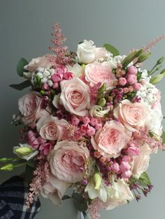 a bouquet of pink and white flowers sitting on top of a wooden table next to a gray wall