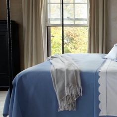 a bed with blue sheets and pillows in front of a window