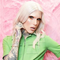 a woman with white hair and tattoos on her arm posing in front of a pink background