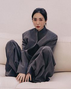 a woman sitting on top of a white couch next to a wall and looking at the camera