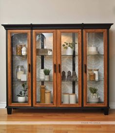 a wooden cabinet with glass doors and shelves filled with pots, plants and other items