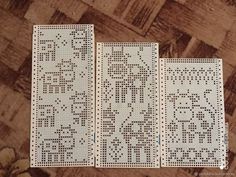 three pieces of cross stitch are laid out on the floor, each with different letters and numbers