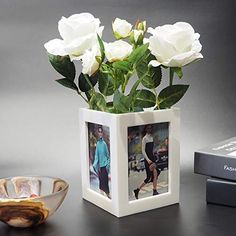 a vase with white roses in it next to a remote control and a photo frame