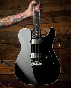 a person holding an electric guitar in front of a wooden wall with flowers on it