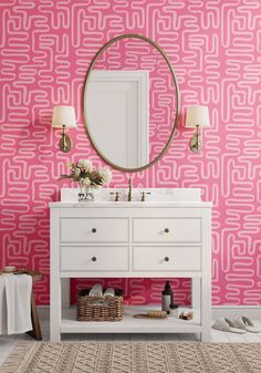 a bathroom with pink and white wallpaper, a round mirror over the sink and two lamps