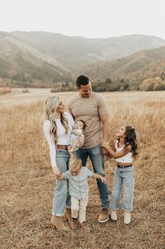 a family standing in a field with mountains in the backgroung and holding hands