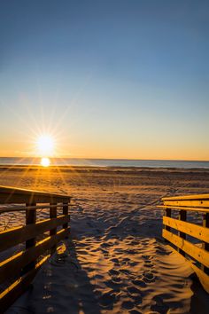 the sun is setting over the beach with wooden benches in the foreground and sand on the ground