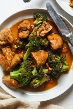 a white plate topped with chicken and broccoli covered in gravy next to a fork