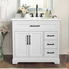 a white bathroom vanity with drawers, mirror and flowers in vases on the floor