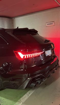 the back end of a black sports car parked in a parking garage with its lights on