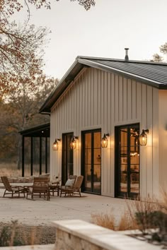 a white house with black doors and lights on the outside, sitting next to an outdoor dining area