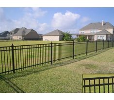 a black fence in front of a house with houses behind it and grass on the ground