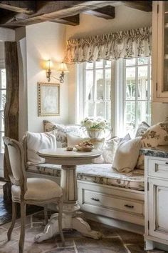 a room with white furniture and lots of pillows on the windows sill, along with an old fashioned dining table