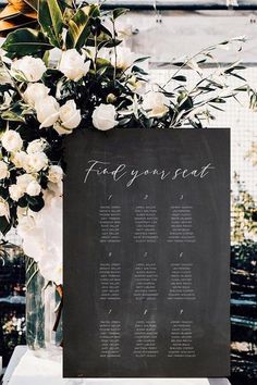 a table plan with white flowers and greenery is displayed in front of a blackboard