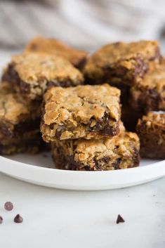 chocolate chip oatmeal cookie bars stacked on a white plate with scattered chocolate chips