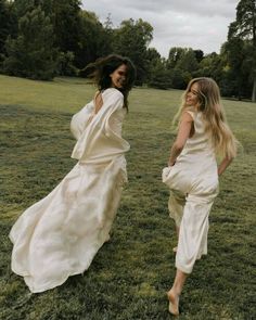 two women in white dresses are walking through the grass