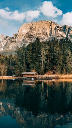 there is a mountain in the background with trees around it and a small cabin on the water