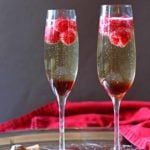 two champagne flutes with raspberries in them sitting on a tray next to crackers