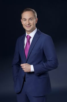 a man in a blue suit and pink tie posing for the camera with his hands on his hips