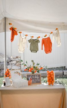 an orange and white baby shower is set up under a tent with clothes hanging from it