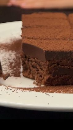 a piece of chocolate cake on a white plate with powdered sugar around the edges