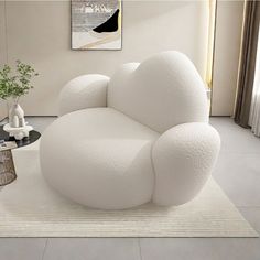 a large white chair sitting on top of a rug next to a vase and table