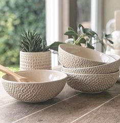 three white bowls and two wooden spoons on a table with plants in the background