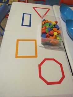 the table is made out of white paper with colorful shapes on it and plastic spoons next to it