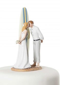 a wedding cake topper with a bride and groom kissing next to a surfboard