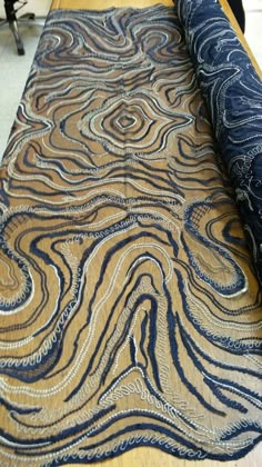 a roll of blue and gold fabric sitting on top of a wooden table next to a chair