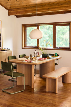 a dining room table with two chairs and a bench in front of a window that overlooks a wooded area