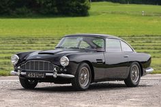 an old black car is parked on the side of the road in front of a green field