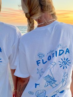 Our EXCLUSIVE Greetings From Florida Sunhoney T-shirt is perfect for beach lovers! This Comfort Colors t-shirt features a playful blue drawn design of popular Florida symbols like the sun, shell, mermaid, and more. Style this shirt over your fave bikini as your new go-to beach tee or style with biker shorts and sneakers for the cutest summer fit! Designed by us, handmade by us in Jacksonville Beach, FL Product is made to order: available for pick up/ships in 2-4 business days Content: 100% Cotto Graphic Tee T-shirt For Family Vacation, Summer Blue T-shirt With Screen Print, Blue Graphic Print T-shirt For Family Vacation, Blue Crew Neck T-shirt For Vacation, Graphic Tee With Custom Print For Vacation, Blue Cotton T-shirt For Family Vacation, Relaxed Fit T-shirt For Family Beach Vacation, White Graphic Tee For Beach Season, Blue T-shirt For Family Vacation In Summer