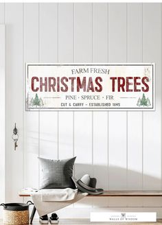 a christmas tree sign hanging on the side of a white wall next to a chair