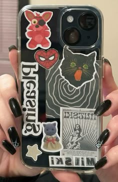 a woman holding up her phone case with stickers on it's back and black nails