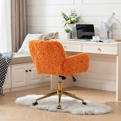 an orange chair sitting on top of a white rug in front of a desk with a laptop