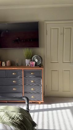 a bedroom with a bed, dresser and flat screen tv mounted on the wall above it