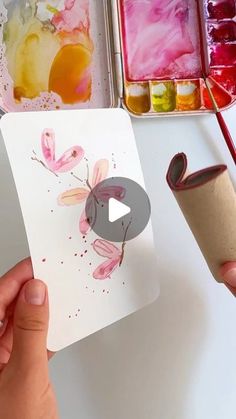 someone is holding up a card with watercolors on it and paper roll in front of them