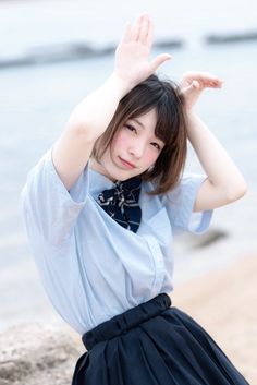 a young woman sitting on top of a beach next to the ocean holding her hands up