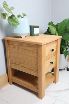 a wooden table with two drawers and a potted plant next to it on the floor