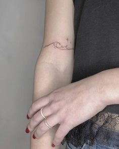 a woman's left arm with a small wave tattoo on her left arm and a diamond ring in the middle