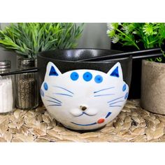 a bowl with a cat's face painted on it sitting next to some plants