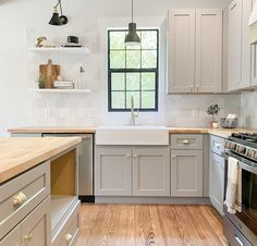 a kitchen with white cabinets and wood floors, an oven, sink, dishwasher and window