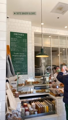 people standing in front of a bakery with food on display behind the counter and menu hanging from the ceiling