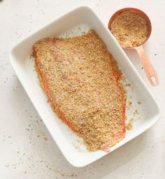 a white plate topped with meat covered in seasoning next to a bowl of sauce