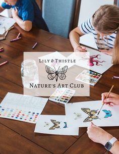 two children sitting at a table drawing with watercolors and pencils on paper