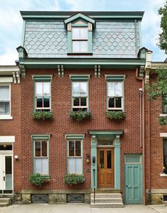 an old brick house with green shutters and flowers on the window boxes in front