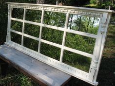 an old window sitting on top of a wooden bench in front of some bushes and trees