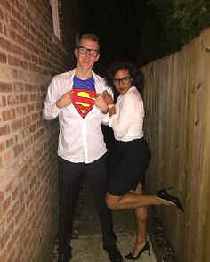 a man and woman standing next to each other in front of a brick wall with a superman t - shirt on