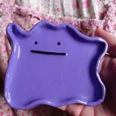 a hand holding a purple plate with a face drawn on the front and back of it